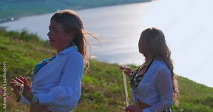Two European women dancing oriental dances on a background of water and green grass