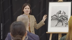 Attractive female auctioneer standing at lectern and presenting photography to audience at art auction
