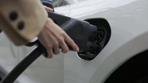 Woman putting charging plug in to socket of electric car