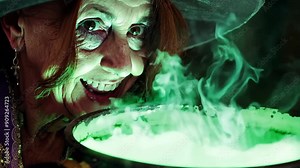 Witch stirring a bubbling cauldron. A witch with a pointed hat and warty nose mixes a potion in a steaming, bubbling cauldron. The green glow of the potion lights her face eerily. Stock Video