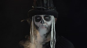 Frightening man in creepy skeleton Halloween cosplay exhaling cigarette smoke from his mouth