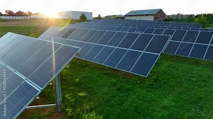 Low angled aerial flyover of solar panels. Solar panels reflect sunlight. Arrays generate electric power to support electricity grid. Green renewable energy.