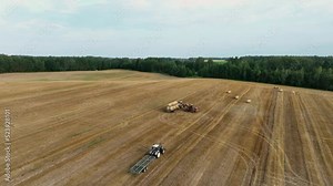Hay Making. Front end loader loads round bales of straw from Hay Trailer. Storage hay at farm. Hay rolls as Forage feed for livestock. Winter Wheat planting, autumn grain harvest, drone view.