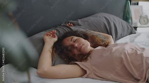 Young beautiful woman falling down on her back on bed with eyes closed and sleeping