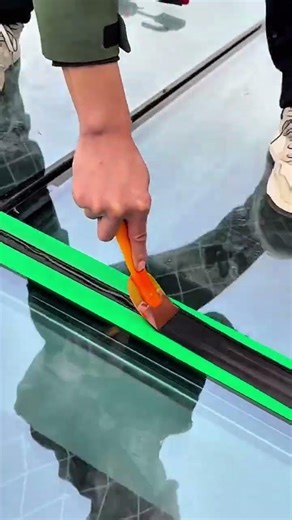 Scraping glass surface clean with orange handheld scraper tool and green edge tape protection