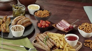 Putting fresh pretzels on table. Traditional German Cuisine. Smoked sausages with fried potatoes, pickled cucumbers, bratwursts. Composition of Cooked National Czech Food.