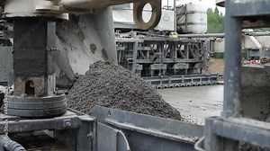 Road paving machine or slipform paver finisher dumping asphalt concrete mass on roadway surface to make screed. Concept of heavy-duty motorized vehicle for highway engineering and construction works.