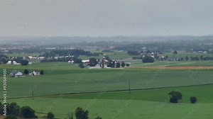 Rainy day with thunderstorm over Rural farm n USA. Barns and silos amidst rolling fields of green crops. Farm buildings and pastures extend into the distance. Descending drone wide shot.
