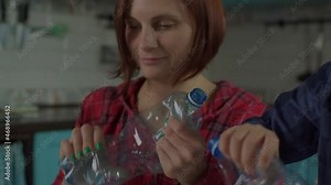 Close up of 30s mother and son sorting recycle waste at home. Family sorting paper, glass and plastic recyclable materials into containers with green recycle sign.
