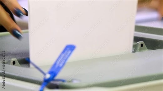Close-up of a man's hands dropping sheets of paper or a ballot into a voting machine.