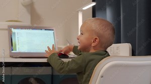Happy toddler child climbing into chair playing with parent laptop on desktop