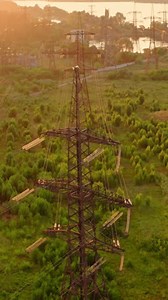 Power line pylons near the river. Electric towers with electric cables with high voltage current. Flight over the transmission lines in the evening. Aerial view. Vertical video