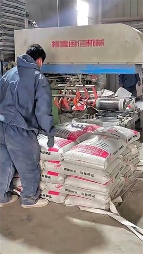 Mechanical arm lowers bag worker watches stack builds red white weight aligns