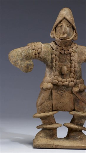 Possibly over 1700 years old, this figure is attributed to the Colima culture of ancient Mexico. It is made of ceramic tanware and features a standing person in an elaborate costume holding rattles. It measures 11.4 x 20.6 x 26.7 cm (4 1/2 x 8 1/8 x 10 1/2 in). This artifact is now housed at the Walters Art Museum in Baltimore, United States. It was acquired by anonymous gift in 2008. | Cosmos University