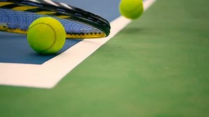Close up of tennis equipment on the court. Sport, recreation concept. Yellow racket with a tennis ball in motion on a clay green blue court next to the white line with copy space and soft focus.