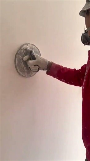 sanding and smoothing a white wall surface using a manual hand sander and wearing protective gear