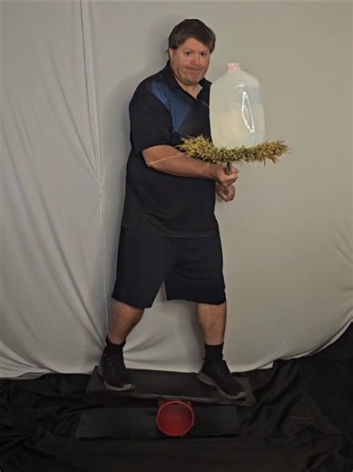 Strength Multitasking Exercise Using Gallon Of Water Balanced On Broom Riding Balance Board