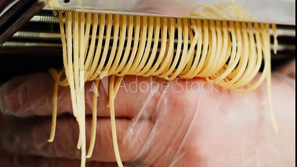 Woman using pasta machine to make fresh pasta dough in the kitchen, cooking in italian restaurant, making noodles.