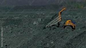 A large truck unloads rock in slow motion. Mining equipment at the bottom of the quarry. Quarry industry footage. Mining of iron ore. Hard work. Metallurgy background for design 4K