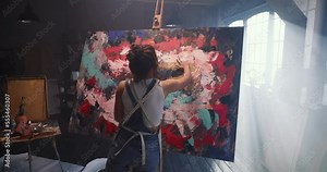 A female artist works on an abstract oil painting, draws with her hands, creating a masterpiece. A talented young artist paints on canvas with her fingers and hands. Contemporary and innovative art.