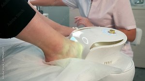 Woman is drying transparent base coal of shellac on nails on toes in UV lamp in beauty salon. Hygiene and care for feet. Professional pedicure in cosmetology clinic.