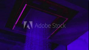 Water flowing from the beautiful modern designed shower . Overhead futuristic , luxury shower in dark bathroom . Pink , purple led lights inside . Unique design . Water falling , dropping , pouring