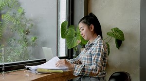 Working outside on a leisurely day at a cafe. Beautiful Asian woman checking a stack of financial documents. with files on laptop computer Validate a small family-owned coffee shop account.