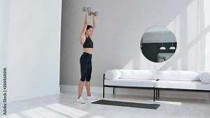 Strong and Fit Beautiful Girl in an Athletic Top is Doing Squat Exercises in Her Bright and Spacious Living Room with Minimalistic Interior.