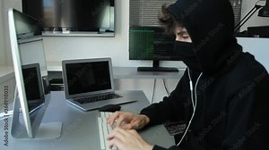 masked hacker using computer to hack data organizing massive data breach attacks on corporate servers located in a secret underground place wearing a black hoodie black cap and a scarf hidde identity