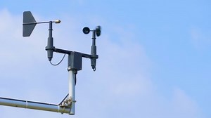 Anemometer and wind vane against blue sky on windy day