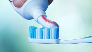 Dental Health - Squeezing toothpaste with colorful stripes from a tube onto a toothbrush.