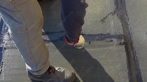 Worker performs sealing overlapping bitumen sheets on the flat roof of the building.