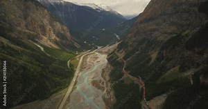 4K Cargo train in Canadian rockies surrounded by Turquoise stream and evergreens- Aerial - Higher elevation