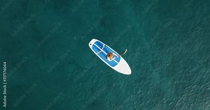 Young woman relaxing floats paddle board on calm surface of sea water top view along coast in Greece at sunset. Summer holiday vacation concept. Wellness woman enjoy outdoor lifestyle and water sports