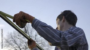 Young Man Measuring with Tape Measure Instrument and Draws Marks With Pencil on Metal Construction in Backyard Garden. Household on Countryside. Spring Evening in Rural Area. 4K 10-bit Hybrid log Gama