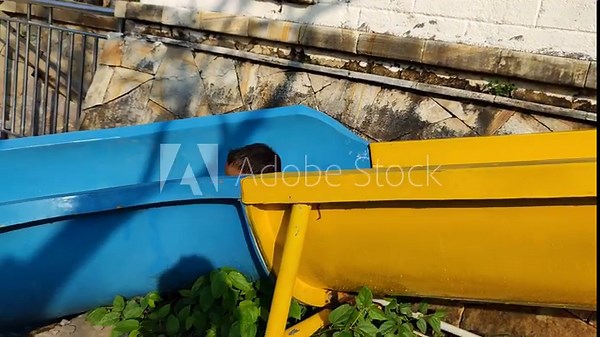 A boy is happily playing on a slide in a swimming pool with his mother