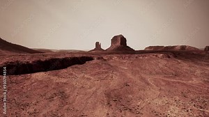 A barren desert landscape featuring a prominent rock formation in the distance under a clear sky.
