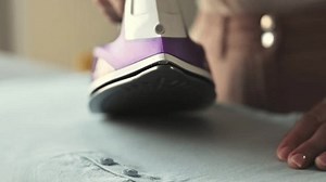 Girl hand using iron with steam mode for wrinkled clothes, closeup view. Woman with hot electric tool smoothing textile