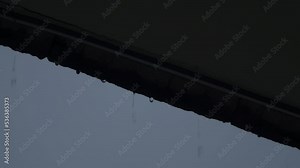 Rain and roof. Falling rain from the roof. Rain drops flow down from a roof down. Raindrop pouring off roof on rainy sky daytime. Weather forecast. Represent lazy and relax or chill out mood tone.