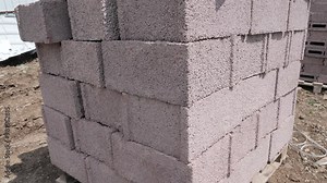 A stack of concrete building blocks sits on a construction site during daytime, ready for use.