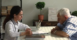 Professional young female therapist general practitioner explaining medical insurance benefits, showing paper contract agreement to interested older mature retired male patient at acquaintance meeting