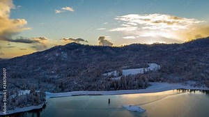 Aerial time lapse in a winter landscape by a lake. Beautiful dramatic view with clouds moving fast, hyper lapse, lots of snow.
