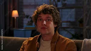 Young man spending evening at home sitting on sofa in living room, switching tv with remote watching program, bored sighing expression, first person pov, close up.