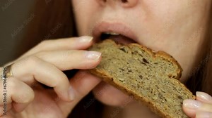 Woman eats a piece of whole grain bread. Portrait close up. Female mouth eating crusty bread.
