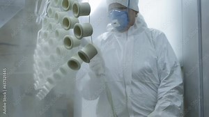 Lamp base painting process at the medical equipment production facility. A worker is using the yellow spray painting tool to color the lamp bases. Medical lamp bases are painted in slow motion.