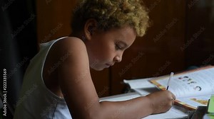 Schoolboy doing homework in his room in the home. Cute african american boy sitting at the table and thinking and writing in his notes. Home education for kids. Boy learning something from his book.