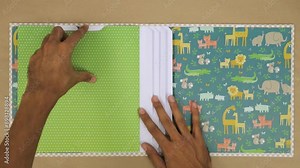 Creating a colorful scrapbook album with baby animal-themed pages and hands placing paper sheets inside