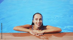 Woman in striped swimsuit emerges from pool water, smiling directly at camera. Concept of summer, joy, and aquatic fun