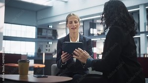 Professional Female Lawyer And Her Assistant Sitting In Modern Diverse Skyscraper Office In Downtown. Two Diverse Women Going Through Schedule and Meetings With Clients On Tablet In Law Firm