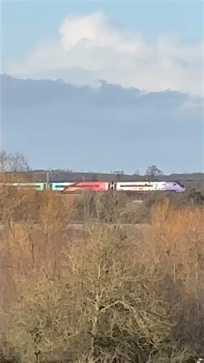 Avanti west coast class 390 pride train passes through trees in the distant countryside #class390
